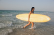 © phocal Media - Expat woman carrying surfboard at sea.