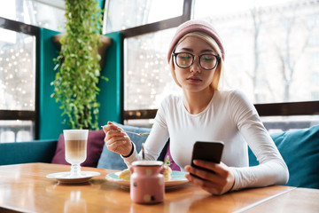 Wall Mural - Young lady using phone drinking coffee while sitting in cafe.