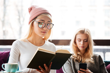 Wall Mural - Young two ladies reading book and using mobile phone.