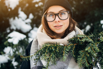 Wall Mural - Close up portrait of a beautiful girl with blue eyes in black glasses in a hat and coat with scarf in the winter park