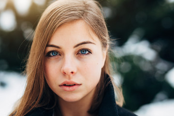 Wall Mural - Closeup portrait beautiful blue eyes girl in black coat walking in winter park