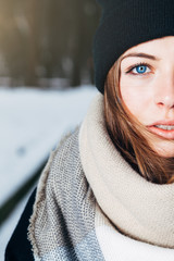 Wall Mural - Portrait of a beautiful girl with blue eyes in a black hat and a scarf in the winter park