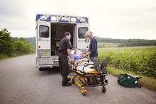 Paramedic And Senior Woman Standing Next To Senior Patient Lying On Stretcher