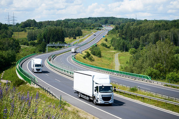 Wall Mural - Two white small trucks driving on the highway with electronic toll gates in a wooded landscape. View from above.