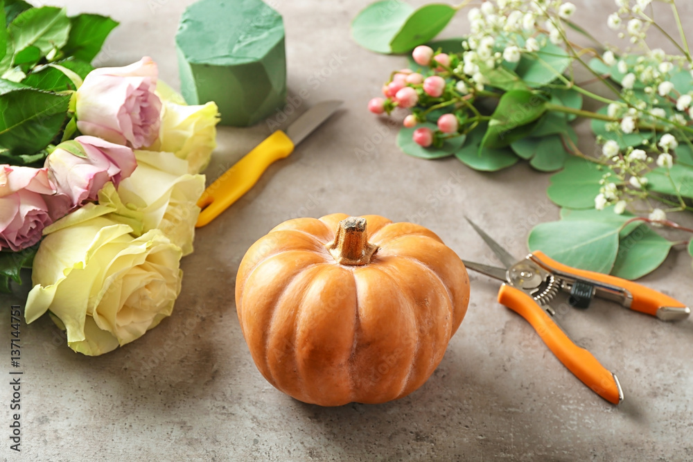 Pumpkin with tools and flowers on gray background