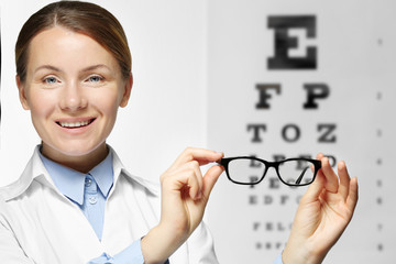 Wall Mural - Young woman holding spectacles on eyesight test chart background