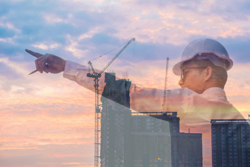 Double exposure man architect pointing at the sky on a wide vision and confidence in the leadership of the city to prosper.Silhouette Building and sunset to  background.