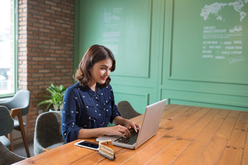 Fototapete - Beautiful cute asian young businesswoman in the cafe, using laptop and drinking coffee smiling