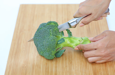 Woman cutting broccoli for cooking on wood block