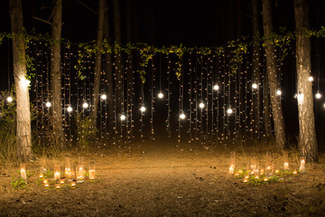 Wedding ceremony evening with candles and lamps in the coniferous pine forest