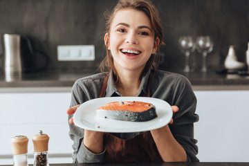 Happy woman standing in kitchen while cooking fish.