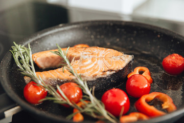 Fish and vegetables on frying pan in kitchen