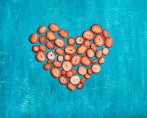 Pieces of fresh red strawberry placed in shape of heart over bright blue painted wooden background, top view, copy space. Love concept. Greeting card for Saint Valentine' s or Lovers' Day