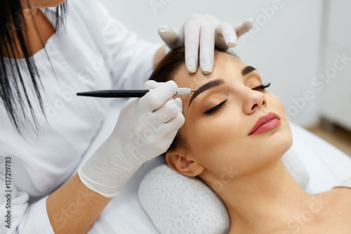Fotografering Beautician Doing Permanent Eyebrows Makeup Tattoo On Woman Face