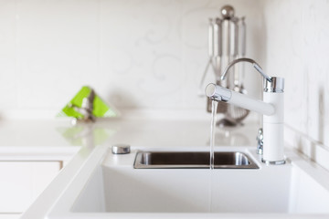 Modern designer chrome water tap over white kitchen sink.