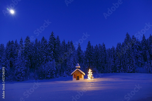 Fotografie, Obraz Illuminated Christmas tree in front of a chapel in winter, Bavaria, Upper Bavari