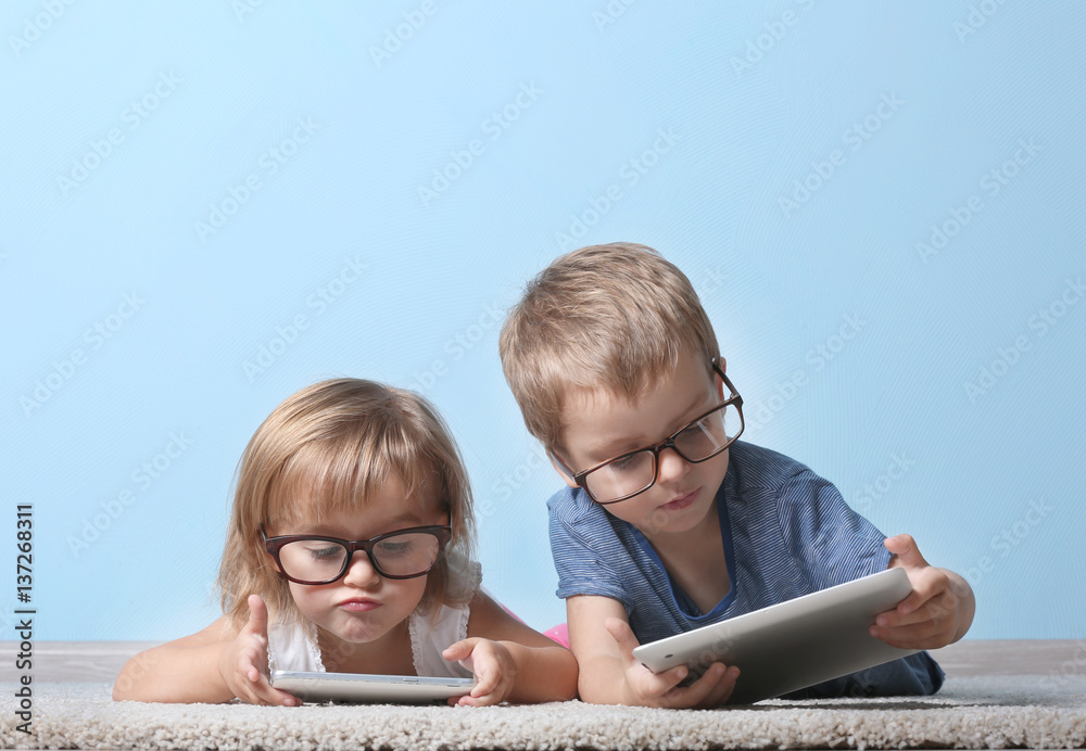 Cute funny children lying on carpet with tablet computer and mobile phone