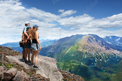Fotografie, Obraz Father with arms around his family looking at beautiful summer mountains landscape, on hiking trip, on top of mountain rock
