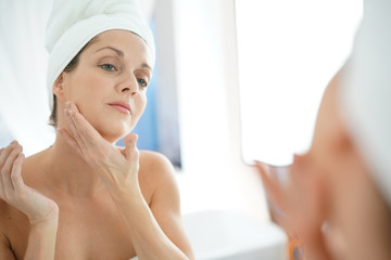 portrait of woman in bathroom applying moisturizing cream