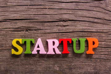 startup word made from colored wooden letters on an old table. Concept