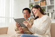 © DragonImages - Joyful Asian woman sitting on sofa with her senior dad and explaining him how to play computer game on digital tablet
