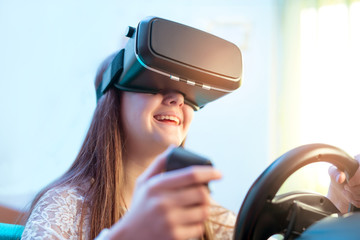 Happy girls in virtual reality glasses playing video game with racing wheels  at home