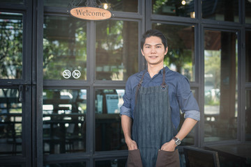 Successful small business owner standing with crossed arms with employee in background coffee shop.