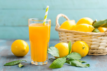 Wall Mural - Lemon juice in glass and fresh fruits with leaves on wooden background, vitamin drink or cocktail