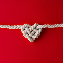 White Rope In Heart Shape Knot On Red Background. Love Concept. Flat Lay.