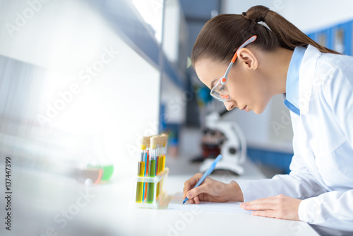 Fotografía side view of scientist writing down test results while working in laboratory
