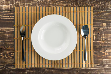 White empty dish with stainless spoon and fork on bamboo weave a