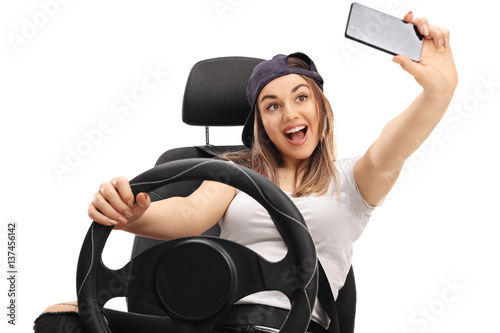 Fotografie, Obraz Cheerful girl sitting in car seat and taking selfie