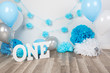 Festive background decoration for birthday celebration with gourmet cake, letters saying one and blue balloons in studio, cake smash first year concept