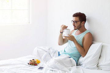 Young man having pancakes in bed and coffee