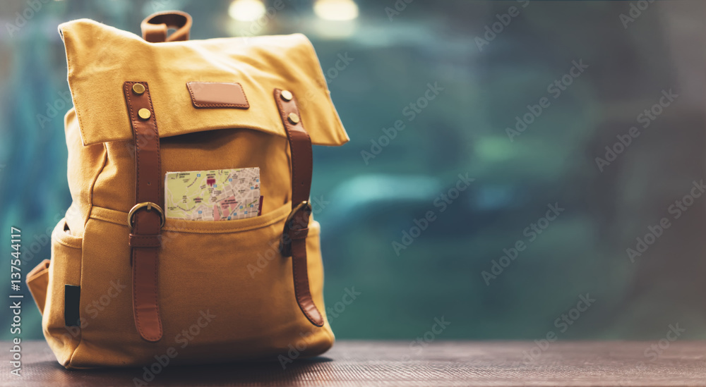 Hipster yellow backpack and map closeup. View from front tourist traveler bag on background blue sea aquarium. Person hiker visiting oceanarium museum in Barcelona on backdrop, blank blurred mockup - obrazy, fototapety, plakaty 