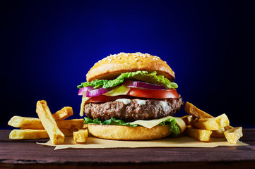 Wall Mural - Craft beef burger and french fries on wooden table isolated on deep blue background.