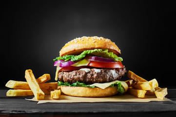 Wall Mural - Craft beef burger and french fries on wooden table isolated on black background.