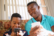 © Diego Cervo - Black Man Teaching Mobile Telephone Technology To Boy At Home