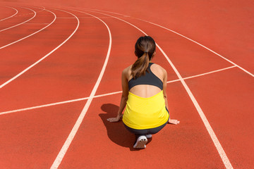Wall Mural - Back view of young woman athlete at starting position ready to start a race. Female sprinter ready for sports exercise on racetrack with sun flare.