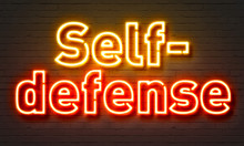 Self-defense neon sign on brick wall background.