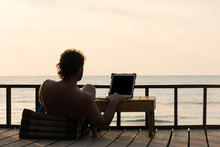 Digital nomad working online on the beach and seeing beautiful sunset.