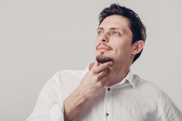 portrait of handsome young pensive man in white shirt on gray ba