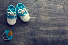 Toned Photo Of Blue Crocheted Child Bootees With Little Nipple On Wooden Background.