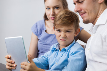 Wall Mural - Frowning little boy holding touchpad with parents