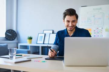 Graphic designer sketching new project on tablet working with laptop in office