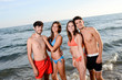 © W PRODUCTION - four happy friends young people man and woman having fun at ocean beach jumping together in the sea