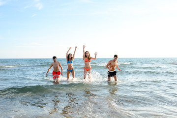 Wall Mural - four happy friends young people man and woman having fun at ocean beach jumping together in the sea