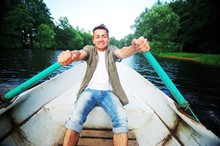 Young Handsome Man Swims On A Wooden Boat And Rowing With Oars