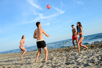 Wall Mural - four young people man and woman playing beach volley together by the sea in sunny summer vacation day