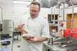 Zufriedener Koch zeigt Schinken vom Schwein in der Keule in seiner Küche